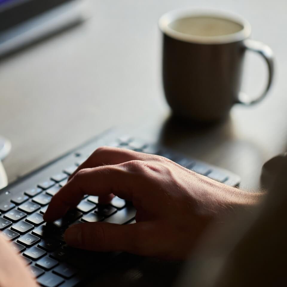 Blurry hand typing quotes near coffee mug shadow